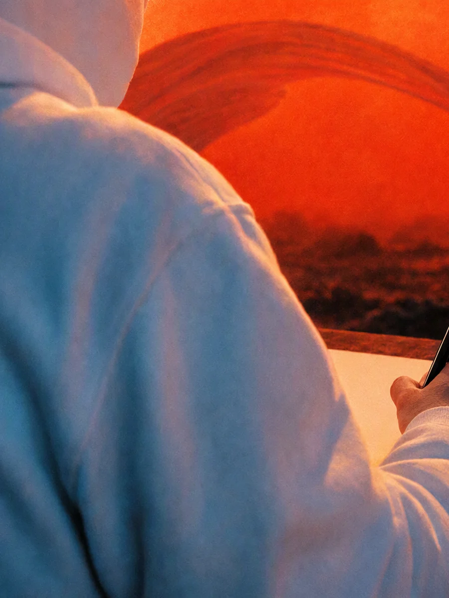 A hand in a pale hoodie sleeve writing on a sheet of paper under a red sky